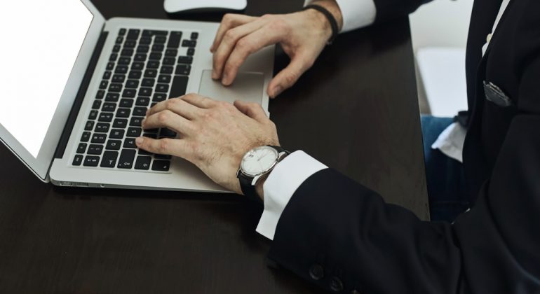Cropped image of a young man working on his laptop , rear view of business man hands busy using laptop at office desk, young male student typing on computer sitting at wooden table